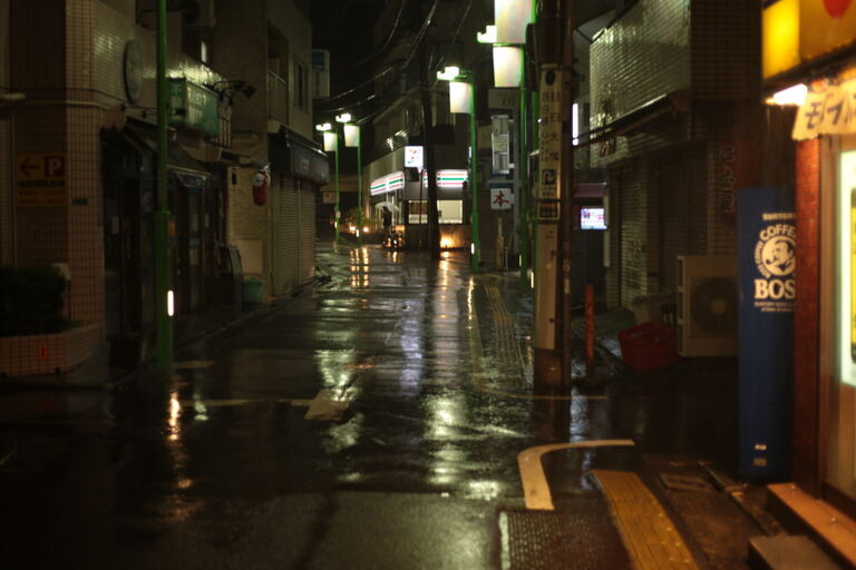 Liminal wet neighborhood street with convenience store glow in the distance